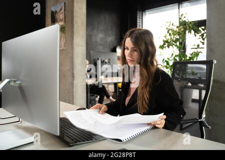 Designerin im Büro, die an einem Architektenprojekt arbeitet. Geschäftsfrau, sehen Sie sich Architekturzeichnungen im Büro hinter dem Schreibtisch an. Architekt Ingenieur arbeitet Stockfoto