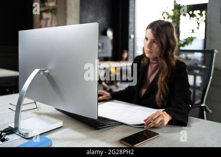 Designerin im Büro, die an einem Architektenprojekt arbeitet. Geschäftsfrau, sehen Sie sich Architekturzeichnungen im Büro hinter dem Schreibtisch an. Architekt Ingenieur arbeitet Stockfoto