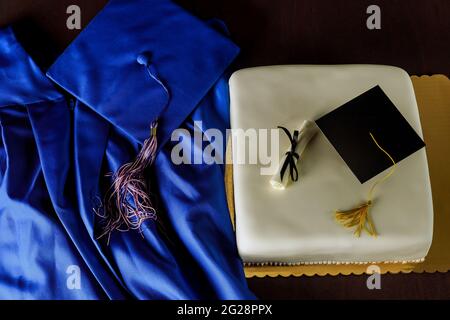 Draufsicht auf blaue Abschlusskleid und Mütze mit Kuchen für Ende der Schule. Stockfoto
