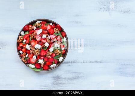 Flatlay eines Tellers mit hausgemachtem frischen Salat aus Babyspinatblättern, geschnittenen Erdbeeren, Walnüssen, Feta-Käse und einem leichten Vinaigrette-Dressing serviert Stockfoto