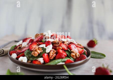 Teller mit hausgemachtem frischen Salat mit Babyspinatblättern, in Scheiben geschnittenen Erdbeeren, Walnüssen, Feta-Käse und einem leichten Vinaigrette-Dressing. Selektiver Fokus mit Stockfoto