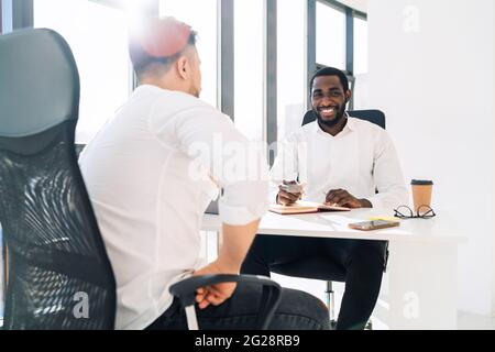 Der Unternehmensleiter führt ein Interview für einen Mann durch. Zwei multirassische Büroangestellte Stockfoto