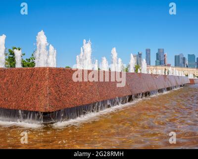 Jets von Springbrunnen an einem sonnigen Tag vor der Kulisse moderner Wolkenkratzer und einem wolkenlosen blauen Himmel. Erholungsgebiet im Victory Park auf Poklonnaya Stockfoto