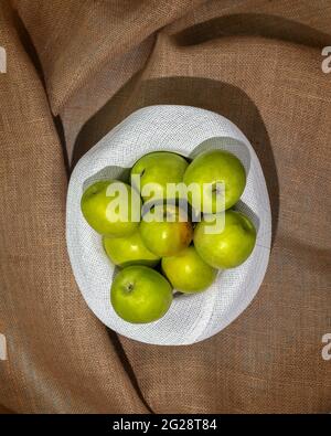 Konzept eines lokalen Marktes, Bauernobst und Erntedankfest, Apfelernte. Reife, grüne Äpfel in einem sommerlichen weißen Hut auf einem textilen Hintergrund Stockfoto