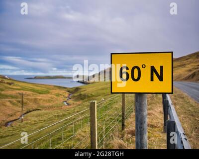 Ein rechteckiges, gelbes Schild mit schwarzen Zahlen auf der A970 auf dem Festland, Shetland, Großbritannien, markiert die 60 Grad nördliche Breitengradlinie. Stockfoto