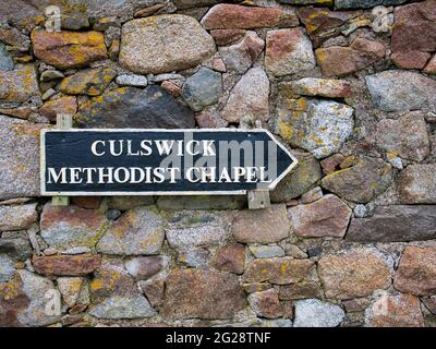 Ein Holzschild an einer bunten, alten Steinmauer weist den Weg zur kleinen, abgelegenen Methodistenkapelle in Culswick, Festland, Shetland, Großbritannien Stockfoto