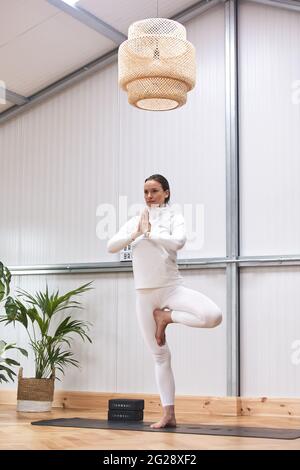 Yogalehrer, der eine komplizierte Körperhaltung in einem gut dekorierten Fitnessstudio unterrichtet. Stockfoto