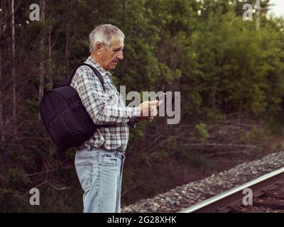 Älterer Mann im karierten Hemd bestimmt die Bewegungsrichtung entlang der Bahngleise auf der Karte auf dem Smartphone-Bildschirm. Stockfoto