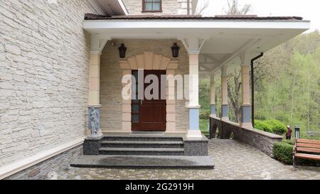 Hölzerne Eingangstür zu einem großen, modernen, eleganten privaten Haus mit Gehwegfliesen und Garten im hinteren Teil. Stockfoto