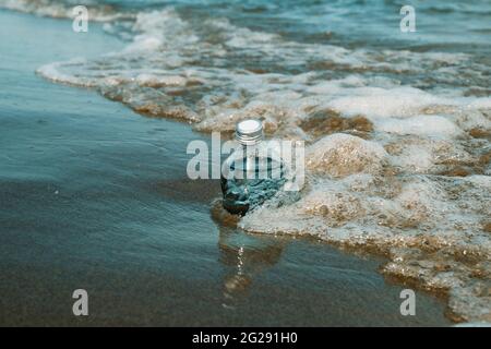 Eine wiederverwendbare Glasflasche an der Küste eines einsamen Strandes, neben einer schäumenden Welle Stockfoto