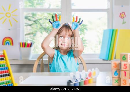 Lustige schöne glücklich Kind Junge zeigt Hände schmutzig mit Farbe. Kind zeichnet lachend mit Farbe. Stockfoto