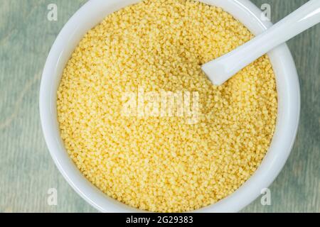 Couscous in weißer Palte. Schließen Sie gelben Couscous auf einem grünen Teller mit Löffel. Flach liegend. Draufsicht Stockfoto