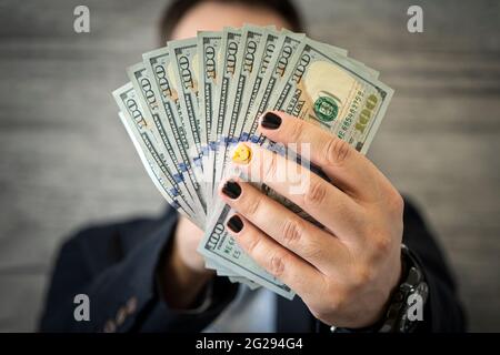 Geschäftsführerin in formeller Klage, die Geld als Bestechung verschenkst. Ein junger Mann mit modisch bemalten schönen Nägeln hält Geld-Cash-Dollars in den Händen Stockfoto