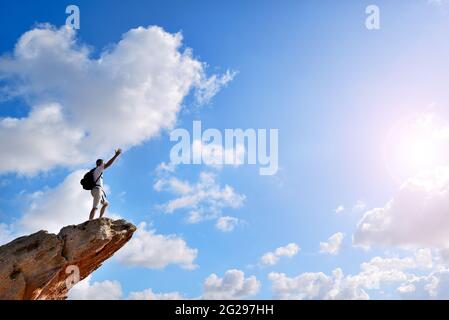 Mann auf einem Felsen, der an einem schönen sonnigen Tag die Arme zum Himmel hebt. Stockfoto