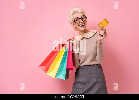 Schöne glückliche Frau hält Einkaufstaschen und Kreditkarte. Foto von gutherzigen älteren Frau auf rosa Hintergrund. Stockfoto