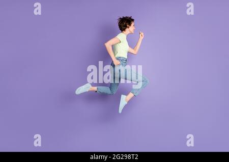 In voller Länge Körpergröße Profil Seitenansicht der schönen fröhlich motivierten Mädchen springen läuft schnell isoliert über violette Farbe Hintergrund Stockfoto