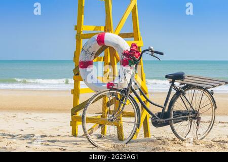 Altes schwarzes Retro-Fahrrad mit Blumenstrauß neben dem Rettungsring Für die Sicherheit des Lebens an der gelben Rettungsschwimmerstation oder Rettungsschwimmerstation Stuhl zum Schutz des Safes Stockfoto