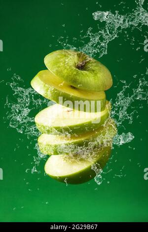 Aufgeschnittener grüner Apfel Schnitt spritzendes Wasser auf grünem Hintergrund Stockfoto