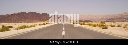 Eine schmale Straße, die zu fernen Bergen führt, in der Arava-Wüste in Israel. Stockfoto
