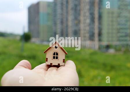 Immobilienmakler, Holzhaus in männlicher Hand auf dem Hintergrund von Wohngebäuden. Kauf oder Vermietung Haus, Wohnen in ökologisch sauberen Vorort Stockfoto