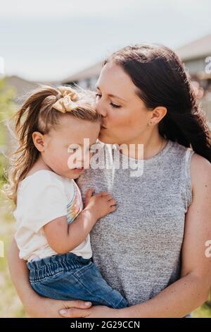 Nahaufnahme der Mutter, die ihre Tochter hält und sie auf die Stirn küsst Stockfoto