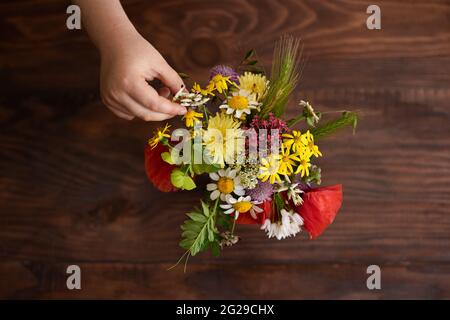 Ansicht von der Decke des kleinen Hands, der im Sommer wilde Blumen in einer Vase platziert Stockfoto