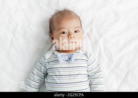 Zwei Monate neugeborener asiatischer chinesischer Junge, der auf seinem Rücken auf dem Bett liegt. Stockfoto