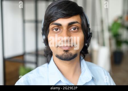 Nahaufnahme eines indischen männlichen Support-Mitarbeiters mit schnurlosem Headset, freundlicher Ostmann mit gemischter Rasse im schicken Casual-Hemd, der die Kamera ansieht, Kopfschuss eines agenten des hindu-Callcenters Stockfoto