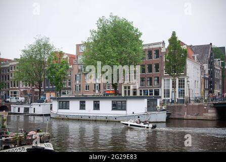 AMSTERDAM, NIEDERLANDE. 06. JUNI 2021. Schöne Aussicht auf Amsterdam mit typisch holländischen Häusern, Brücken und chanel. Kleine Boote auf dem Damm Stockfoto