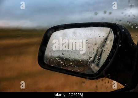 Regentropfen, die sich auf dem Rückspiegel eines Autos auf einem Feld spiegeln Stockfoto