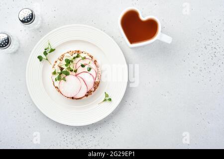 Knusprige Buchweizenbrot-Torte glutenfrei mit Frischkäse, rotem Rettich und Microgreen für ein gesundes Frühstück auf grauem Steingrund. Blick von oben. Stockfoto