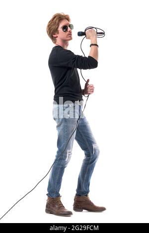 Cool Rocker männlich mit Sonnenbrille hält Mikrofon. Seitenansicht. Ganzkörperlänge isoliert auf weißem Hintergrund. Stockfoto