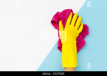 Womans Hand in gelben Gummi-Handschuh wischen durch Lappen auf blauem Hintergrund Stockfoto