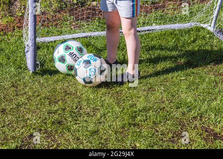 Nahaufnahme der Füße des Kindes in der Nähe von zwei Bällen im Hintergrund des Fußballtals. Stockfoto