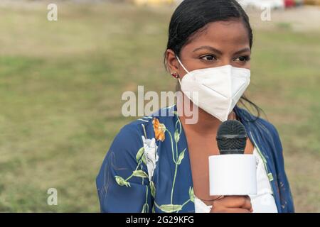 Reporterin trägt Maske und spricht über das Mikrofon, während sie auf steht Straße in der Stadt Stockfoto