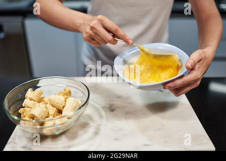 Frau, die Eier für ein Bananenpfannkuchen-Rezept hastert Stockfoto