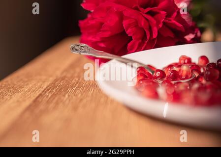 Rote Granatapfelkerne auf einem silbernen Löffel auf einem Porzellanteller Stockfoto