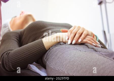 Eine Patientin auf dem Untersuchungstisch im Ultraschalldiagnoseschrank. Eine Frau liegt auf einer Couch mit gefalteten Händen auf dem Bauch und wartet auf ein besonderes Stockfoto