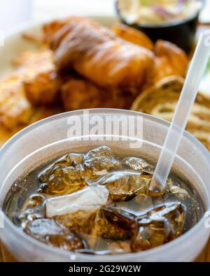 Selektive Konzentration auf ein hohes Plastikglas mit Limonade mit Eis und Stroh. Mahlzeit im Hintergrund verschwommen. Diner-Einstellung. Stockfoto