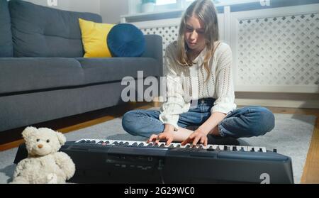 Teenagermädchen, die auf dem Boden sitzt und Klavier spielt. Stockfoto