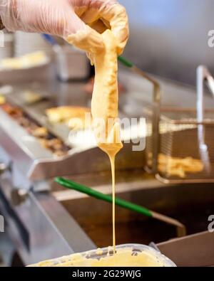 Ein Koch taucht ein Stück Fisch in den Teig, bevor er den Fisch in einer heißen Ölfryer kocht. Stockfoto