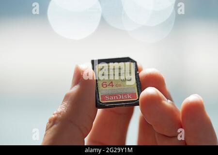 Finger, die eine SanDisk SD-Speicherkarte gegen einen unscharf abgelegten Hintergrund halten. SanDisk ist ein Produkt der Marke Western Digital. Stockfoto