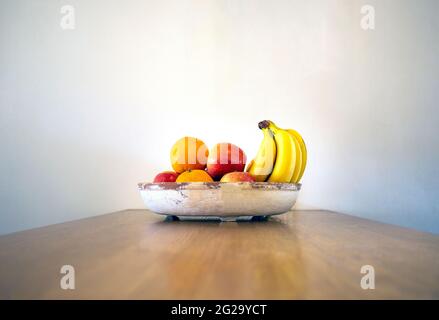 Gesunde Obstschale auf Holztisch mit Bananen, Orangen und Äpfeln an der weißen Wand modernes Design auf Holztisch, kopieren Raum gesundes Stillleben Stockfoto