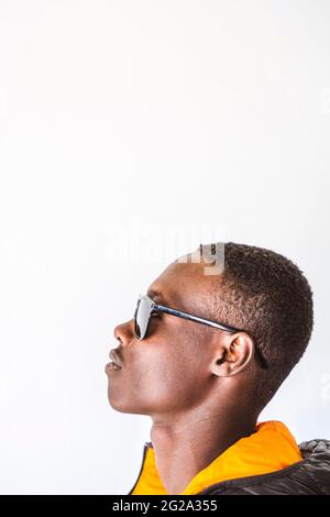 Seitenansicht eines trendigen afrikanischen Mannes in Sonnenbrillen, der gegen eine weiße Wand steht Stockfoto