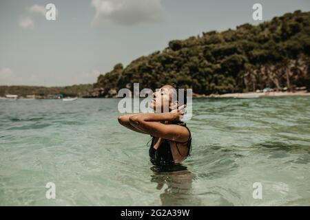 Seitenansicht von jungen ethnischen Frauen in frischem, kühlem Wasser der tropischen Lagune im Sonnenlicht, Bali Stockfoto