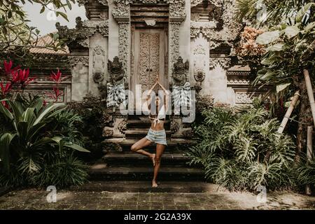 Attraktive, konzentrierte ethnische Frauen, die Yoga-Pose machen und allein vor dem Tempel in Bali meditieren Stockfoto