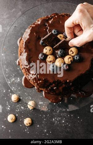 Von oben Ernte unkenntlich Person mit Schokolade Keks für die Dekoration hausgemachten Kuchen mit Schokolade Ganache und Beeren bedeckt Stockfoto