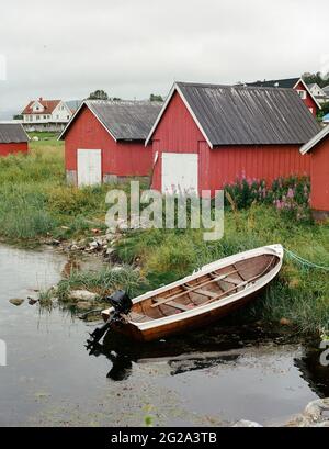 Holzboot mit Motor an der grasbewachsenen Küste des Sees in der Nähe von roten Scheunen in einem wunderschönen Dorf Stockfoto