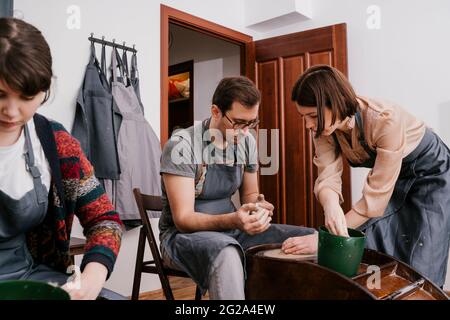 Begeisterte Menschen in Schürzen arbeiten mit Ton Bildhauerei auf Töpferscheibe mit Hilfe von Handwerkern in großen Licht-Werkstatt Stockfoto