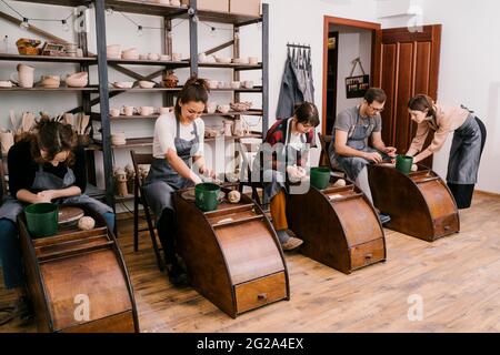 Begeisterte Menschen in Schürzen arbeiten mit Ton Bildhauerei auf Töpferscheibe mit Hilfe von Handwerkern in großen Licht-Werkstatt Stockfoto